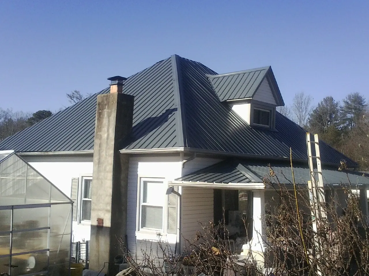 Dark blue standing seam metal roof on a white farmhouse with dormer — Slate & Tile Roof Repair by Roofing Brothers in Creston