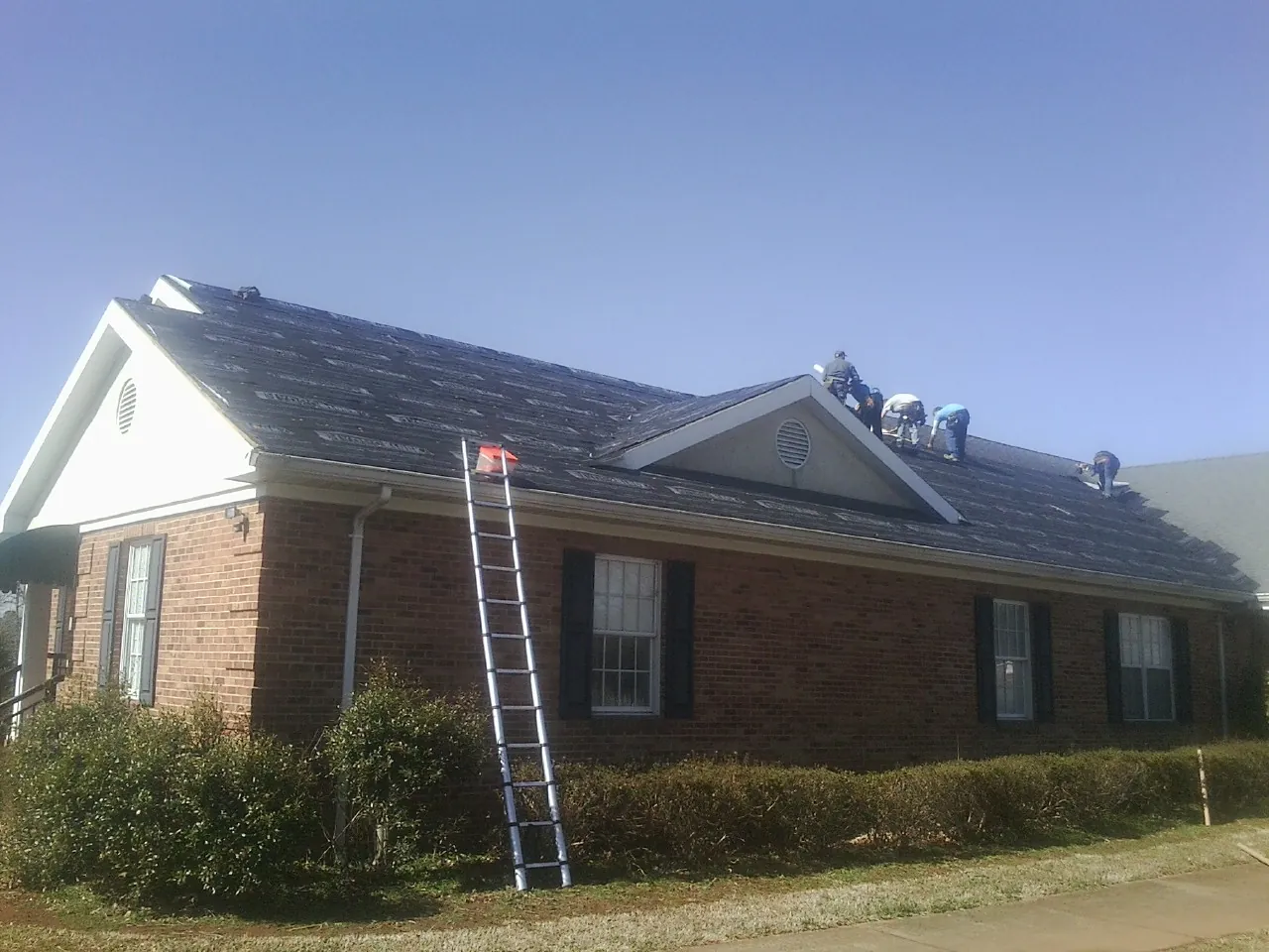 Crew tearing shingles off a brick ranch roof with a ladder set — Metal Roof Repair work by our crew in Creston