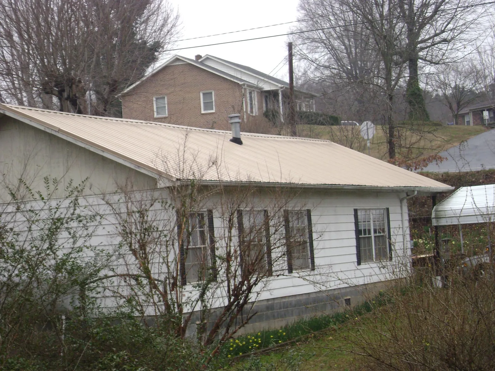 Tan metal roof on a white sided house set into a hillside — Commercial Roofing by Roofing Brothers in Creston