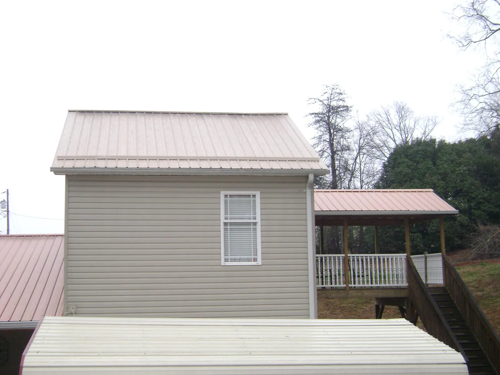 Tan metal roofs on a two story addition and attached porch, from a Roof Replacement job in Creston
